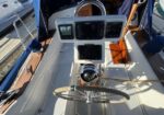 Cockpit helm of a sailboat with a stainless steering wheel and a pedestal holding multiple navigation screens and a compass, wood deck around.