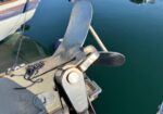 Boat anchor attached to a docked boat, metal fluke visible over calm blue water.