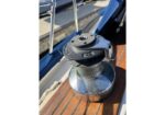 Steel deck winch on a sailboat used for trimming lines, mounted on varnished wood with stainless hardware and a handle slot on top