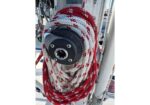 Red-and-white braided rope coiled around a black winch on a sailboat mast, with rigging in the background.