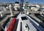 View from the bow of a sailboat at a marina, with nearby yachts, docks, lines, and a row of red fuel containers on the port side.