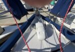 View down onto the bow of a sailboat, with a white windlass/deck hardware in the center and red lines running along the sides toward the cockpit area.