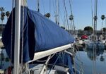 Blue sail cover wrapped around a sailboat at a marina, with palm trees in the background.