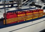 Row of red and yellow life rafts in a wooden cradle attached to the deck of a sailboat.