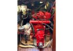 Red diesel engine in a boat engine room with hoses and wiring surrounding it.