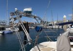 Stainless steel tuna tower and radar dome on a docked boat, with a marina of moored sailboats in the background.