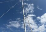 Sailboat mast and rigging rising against a blue sky with white clouds.