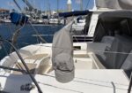 White sailboat cockpit in a marina, with a gray cover over equipment and rigging, other boats and masts in the background.