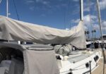 Sailboat docked at a sunny marina with its mainsail furled and covered.