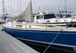 Blue sailboat moored at a marina, beige deck, white cabin, with other sailboats in the background.