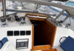 Sailboat cockpit with an open wooden hatch to the cabin and deck hardware like winches and coiled ropes nearby.