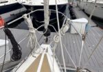 Bow of a sailboat at a marina, with white coiled lines and rigging tied around the bow, dock planks in the background