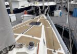 Deck view of a sailboat at a marina, showing a hatch, winches, lines, and other moored boats nearby.