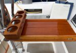 Wooden fold-out serving tray with four circular cup holders mounted on a boat, resting on a teak surface.