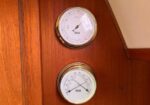 Two round white-dial nautical gauges mounted on a wood wall, one above the other.