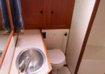 Small bathroom with a round stainless steel sink, chrome faucet, and wooden cabinets above; towels hang nearby and a toilet is tucked behind the counter.
