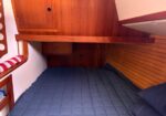 Wooden boat cabin with built-in storage and a blue quilted bedspread.