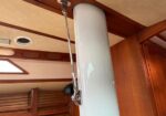 Inside a boat cabin, a pale blue pillar with a metal support strut attached to the ceiling, surrounded by wood paneling and cabinetry.
