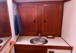 Wooden bathroom vanity with an oval metal sink, mirrored cabinet above, towel hanging on a hook, and a soap dish on the counter.