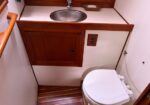 Compact bathroom with wooden vanity, round metal sink, and a closed cabinet next to a white toilet.