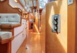Warm wooden interior of a sailboat cabin with cushioned seating and built-in storage along a narrow passageway