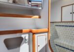 Interior of a small boat cabin with wooden steps, white walls, and built-in storage cabinets beside a tiled seating area with blue trim.