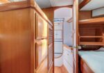 Wood-paneled boat cabin with a bunk bed on the right and a doorway opening to a bright corridor ahead.