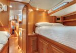Wood-paneled boat cabin with a top bunk bed, built-in storage drawers, and a narrow hallway