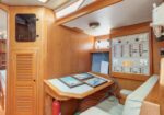 Wood-paneled boat navigation station with a chart table, framed charts, and an electrical control panel on the right, plus a cushioned bench partly visible.