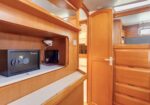 Wood-paneled boat cabin with a black electronic safe on a shelf, wires nearby, and a doorway leading to another compartment.
