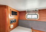 Interior of a small boat cabin with wooden walls, a rectangular porthole window, and a control panel with knobs.