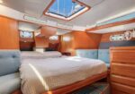 Sailing yacht cabin with a large bed, wooden cabinetry, and blue upholstered seating in a sunlit space.