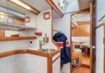 Inside a small sailboat cabin: compact galley with sink, wooden cabinetry, and a navy life jacket hanging on a hook.