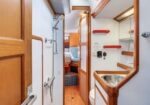 Narrow boat interior hallway with wooden trim; left shows a shower, right has a sink and mirror, leading toward a small cabin.