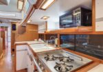 A yacht galley with a four-burner stove, double sink, and wooden cabinetry along a narrow counter run.