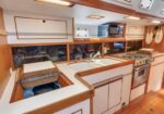 Boat galley kitchen with white cabinets, wooden trim, double sink, stove and oven, microwave, and porthole windows.