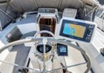 Boat helm with stainless steering wheel, GPS/chartplotter display, compass, and engine control panel, open hatch to cabin behind.