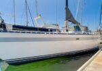 S white sailboat moored at a marina, dock beside calm water, with rigging and sails covered.
