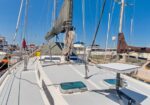 View of a sailboat deck at a marina with sails furled, rigging, and other boats in the background.