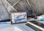 Framed photo resting on a boat’s deck amid rigging and sailing hardware.