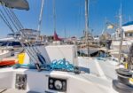 View from the deck of a sailboat in a crowded marina, with coiled blue rope, winch, and multiple masts and boats surrounding the scene.