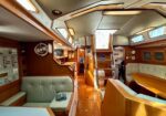 Cozy wooden sailboat cabin with beige cushioned seating, a central dining table, and stairs up to the deck.