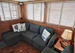 Cozy cabin living area with an L-shaped gray sofa, nautical pillows, wood-paneled walls, and horizontal blinds of the windows.