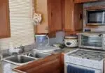 Cozy kitchen with wooden cabinets, a double sink, and a granite counter. Small appliances: toaster oven, microwave, blender pitcher, and a stove with a blue towel on the oven door.