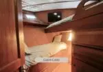 Wood-paneled guest cabin with a lower bed and an upper bunk; built-in storage, small window, and a TV mounted on the wall outside the bed area.