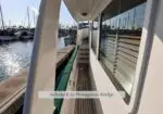 Narrow sidedeck of a white boat at a marina, with cabin windows and moored sailboats in the background; label reads 'Sidedeck to Portuguese Bridge'.