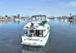 White motorboat named 'POMPANO' cruising in a calm marina with houses and palm trees in the background