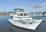 White motor yacht docked in a calm marina with waterfront buildings in the background; speech bubble promotes it as an excellent cruiser and liveaboard, with owner relocating soon.