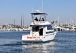 White motor yacht with two decks cruising in a marina; two people on the upper deck, name Samba Pa Ti visible on stern.