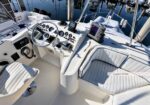 Boat cockpit with steering wheel, gauges, navigation display, and cushioned seating; marina water in the background (Upper Helm area).